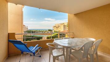 A balcony with a table and chairs, a blue chair, and a view of buildings and a pool.