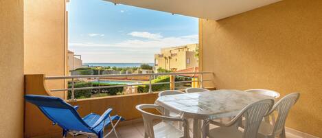 Un balcón con mesa y sillas, una silla azul, y vistas a edificios y una piscina.