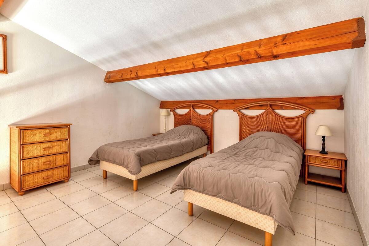 Ein Schlafzimmer mit zwei Einzelbetten, einer Holzkommode und einem Nachttisch mit Lampe.