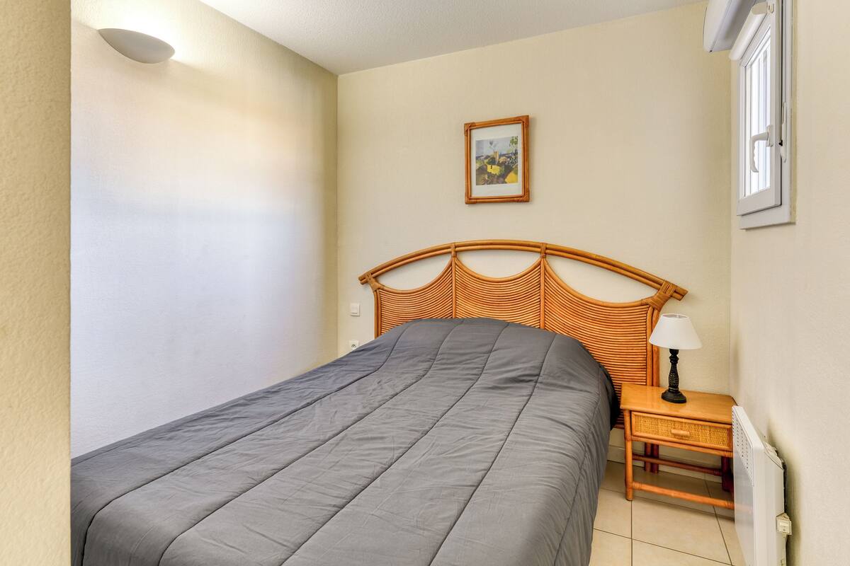 Ein Schlafzimmer mit einem Bett, einem Nachttisch, einer Lampe, einem Bild an der Wand und einem Fenster.