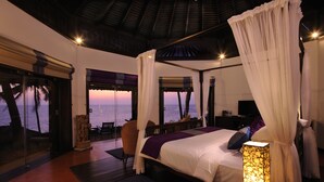 Un dormitorio con cama, mesita de noche, lámpara, sillón y vistas al océano.