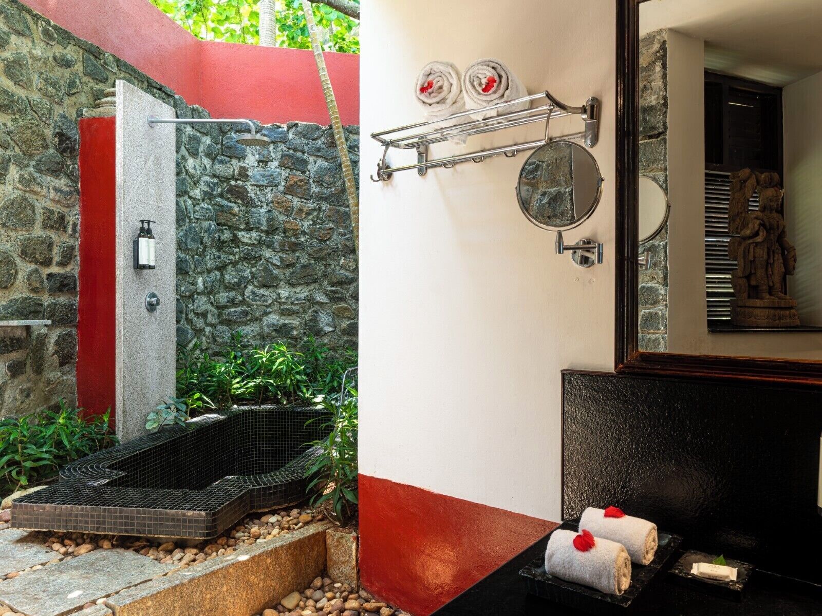 A stone wall with a red vertical stripe, a metal towel rack with towels, a mirror, and a statue.