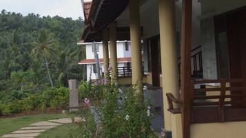 A two-story building with a tiled roof, a balcony, and a garden with palm trees and flowers.