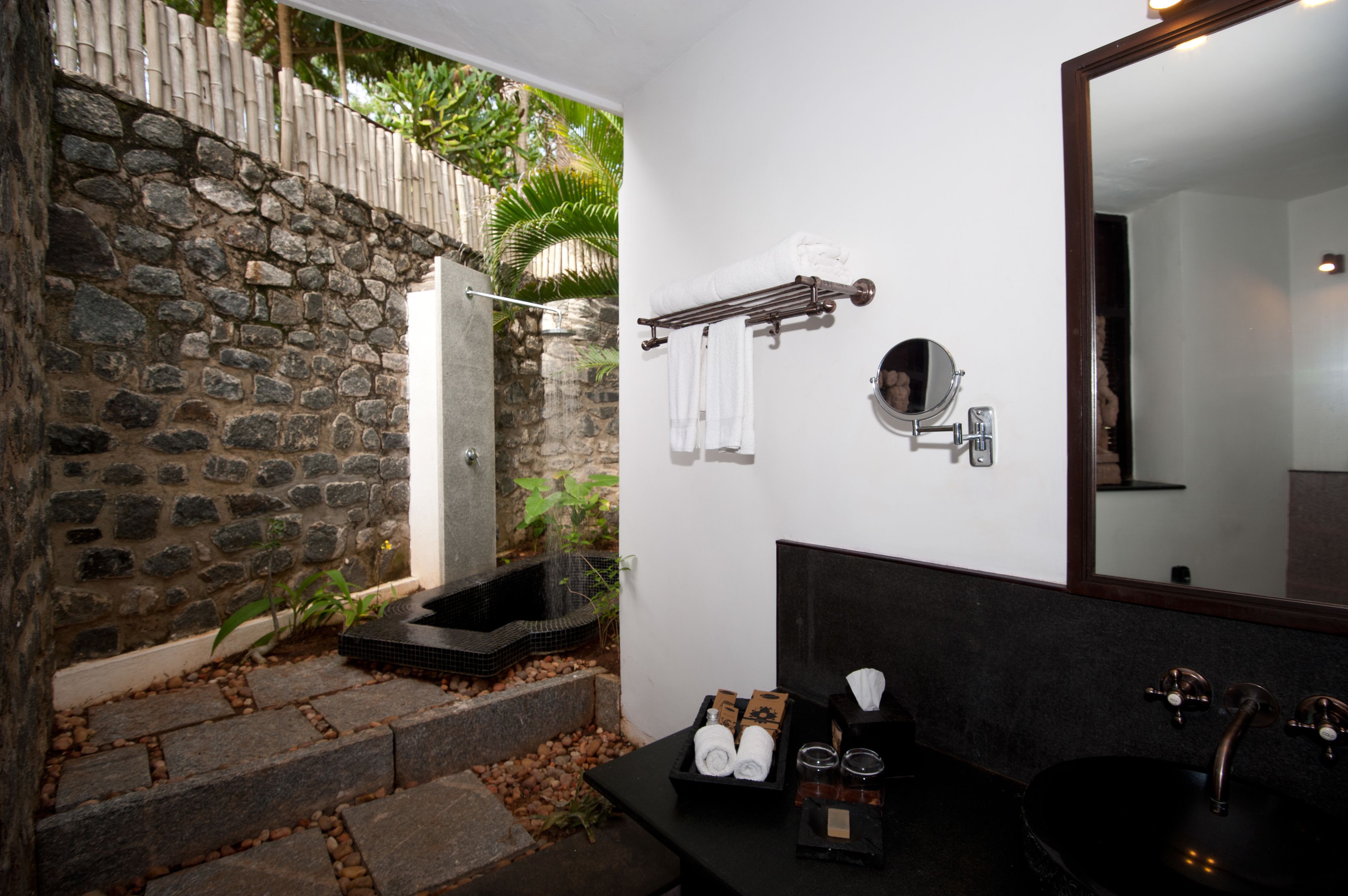 Un baño con pared de piedra, un lavamanos negro y un espejo.