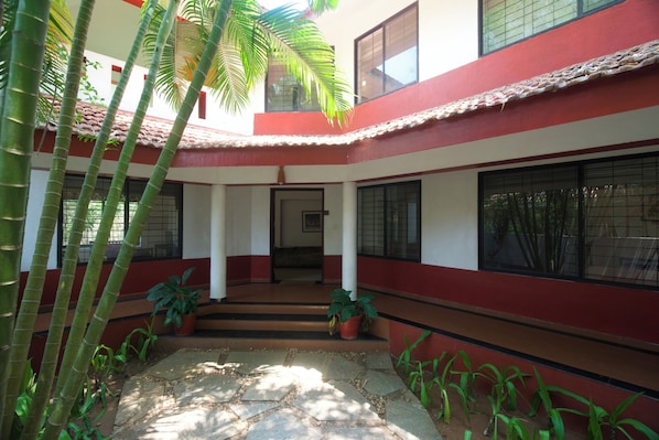 Un patio con un edificio rojo y blanco, plantas en macetas y una escalera que conduce a un nivel superior.