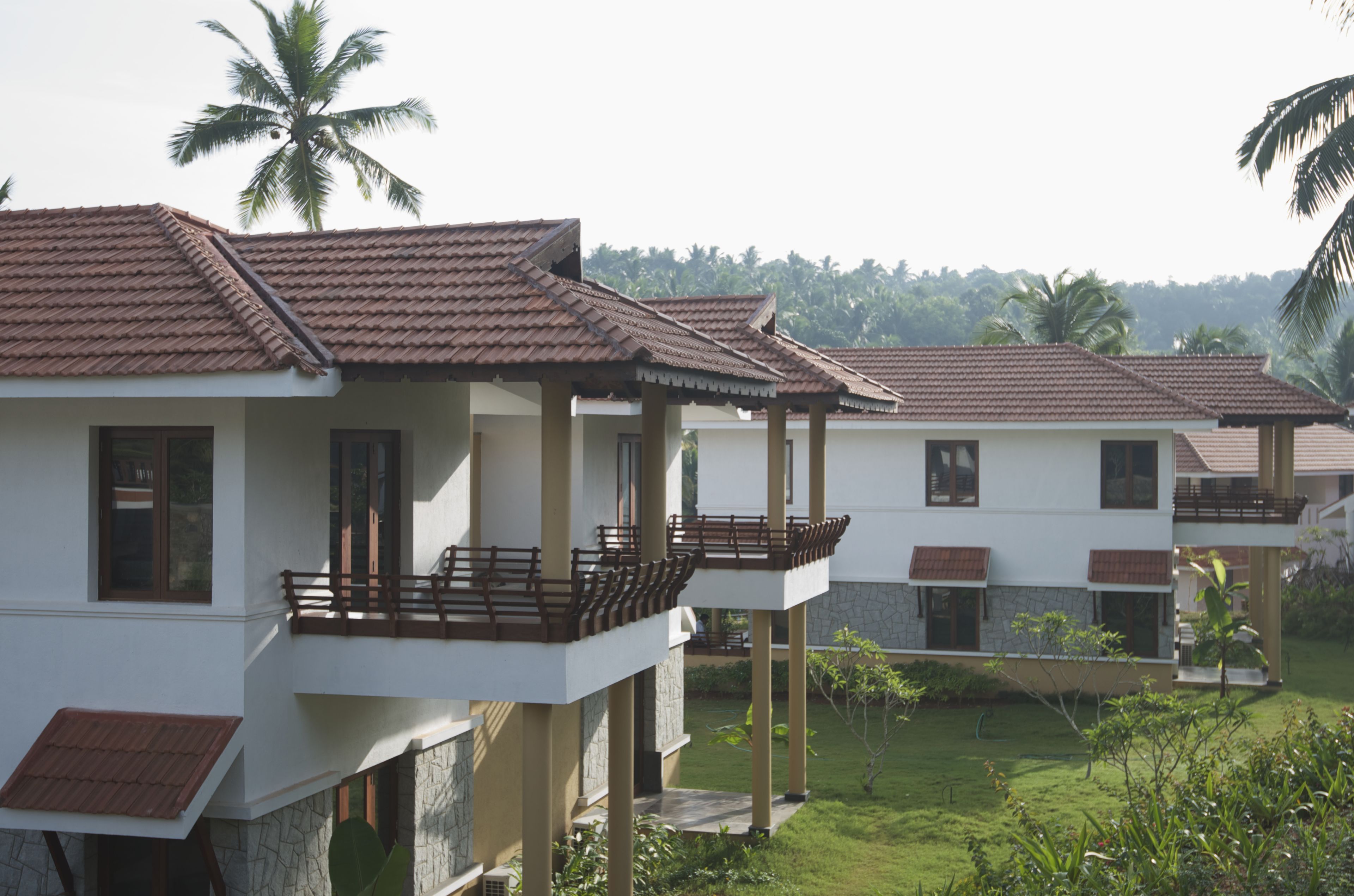 A row of modern villas with balconies, a stone facade, and a lush garden.