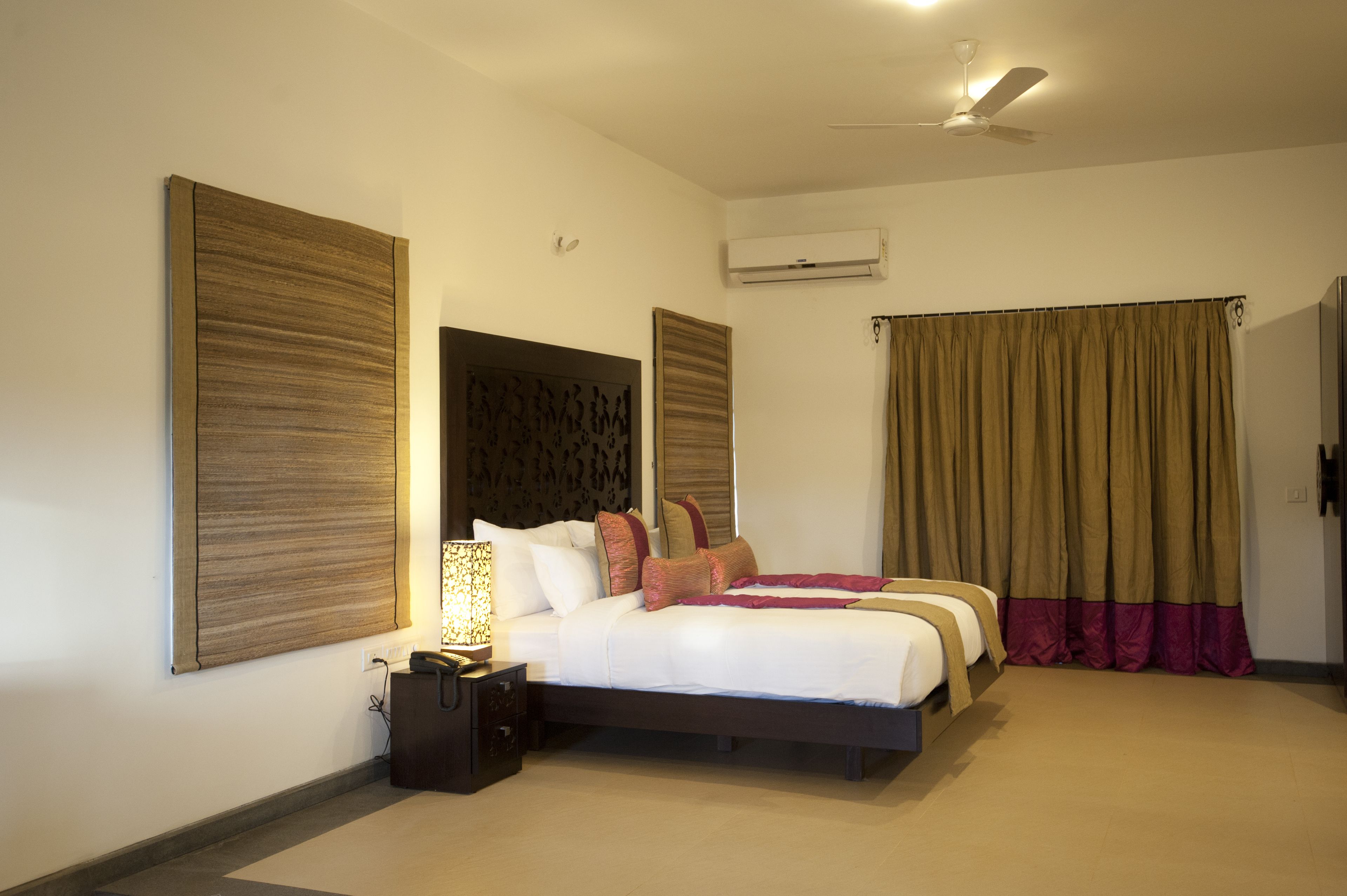 Una habitación de hotel con una cama grande, una mesita de noche con lámpara, ventilador de techo y aire acondicionado.