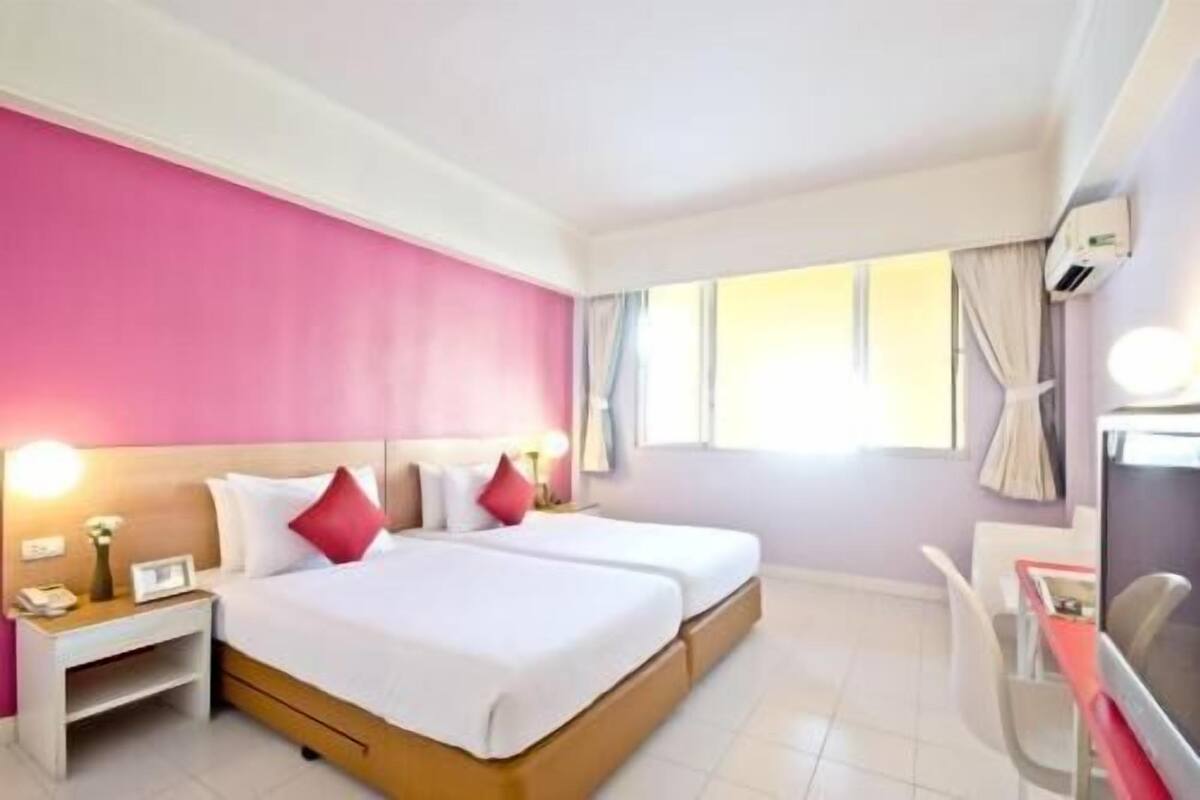 Quarto de hotel com cama, mesas de cabeceira, escrivaninha e televisão.