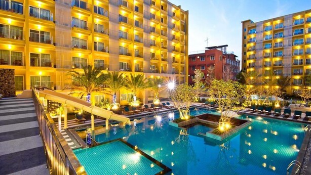 A hotel with multiple balconies, a swimming pool, and palm trees. - Bella Express (Pattaya)
