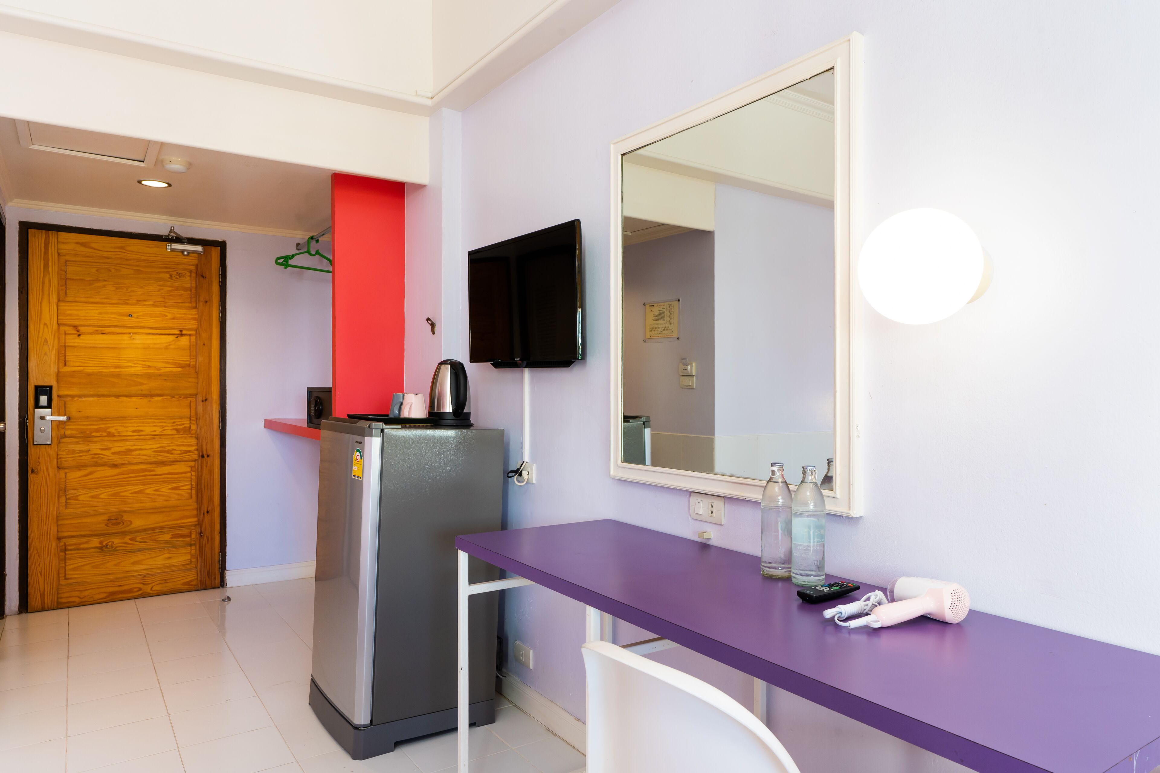 A compact room with a purple table, a refrigerator, a wooden door, and a mounted TV.