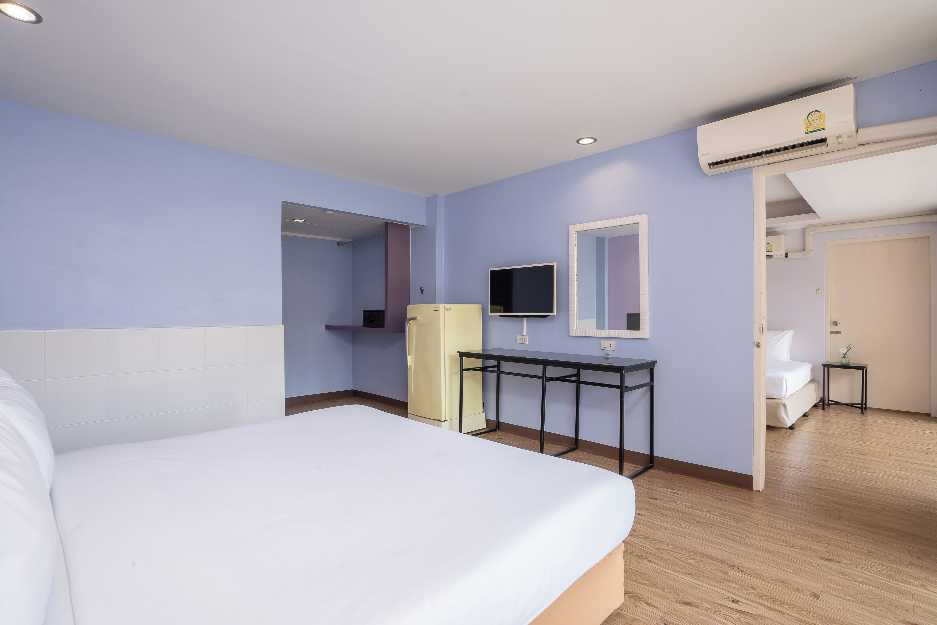 A hotel room with a bed, a small desk, a television, and an air conditioning unit.