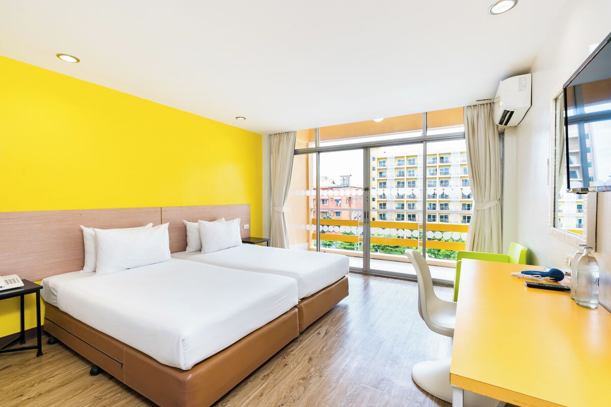 A hotel room with a large bed, a desk, and a view of a building through the window.