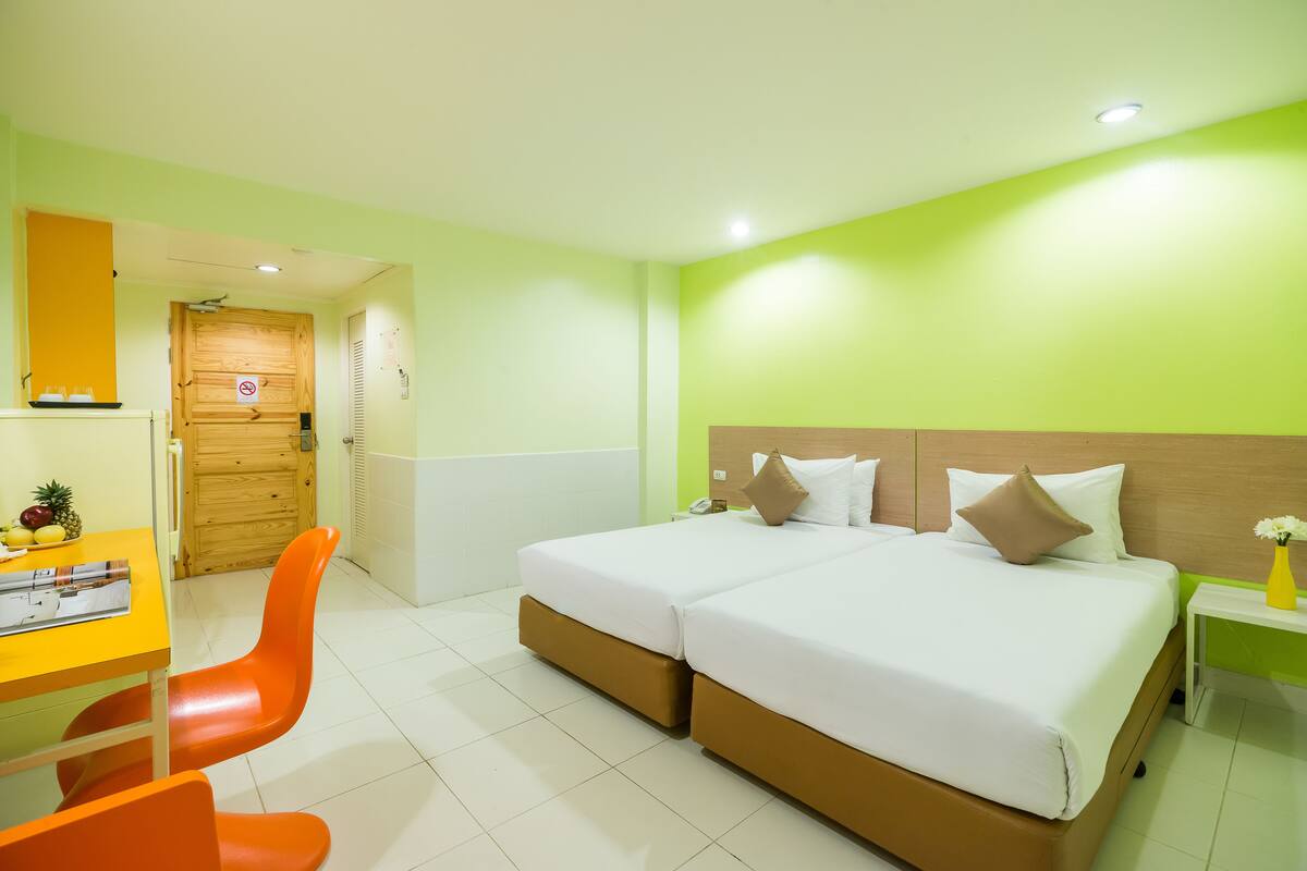 Quarto de hotel com cama de casal, uma escrivaninha com cadeira e porta de madeira.
