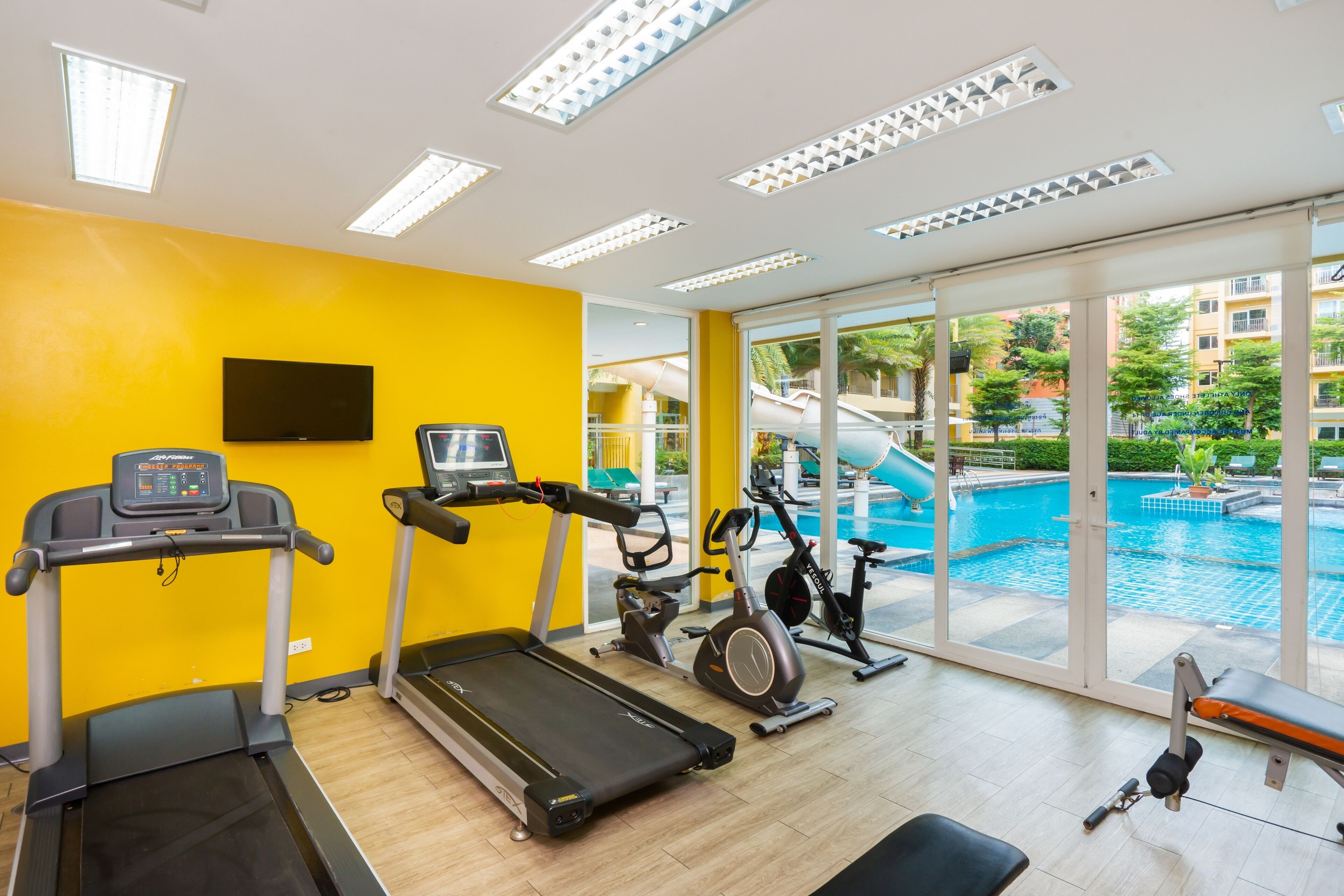 Une salle de sport équipée de tapis de course, d’un vélo elliptique et d’un vélo d’appartement, avec vue sur une piscine.