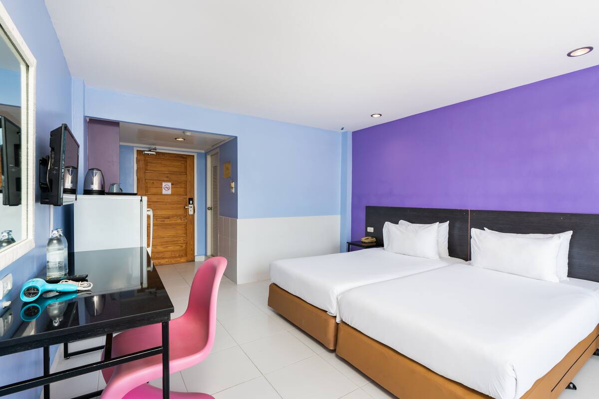 Quarto de hotel com cama, escrivaninha, cadeira e cozinha compacta.