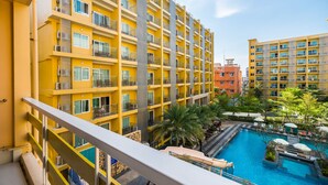 A multi-story hotel with balconies, a swimming pool, and surrounding greenery. - Bella Express (Pattaya)