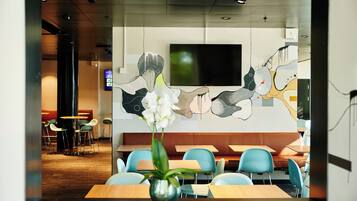 A modern restaurant with a large TV screen, blue chairs, and a vase of flowers on the table.