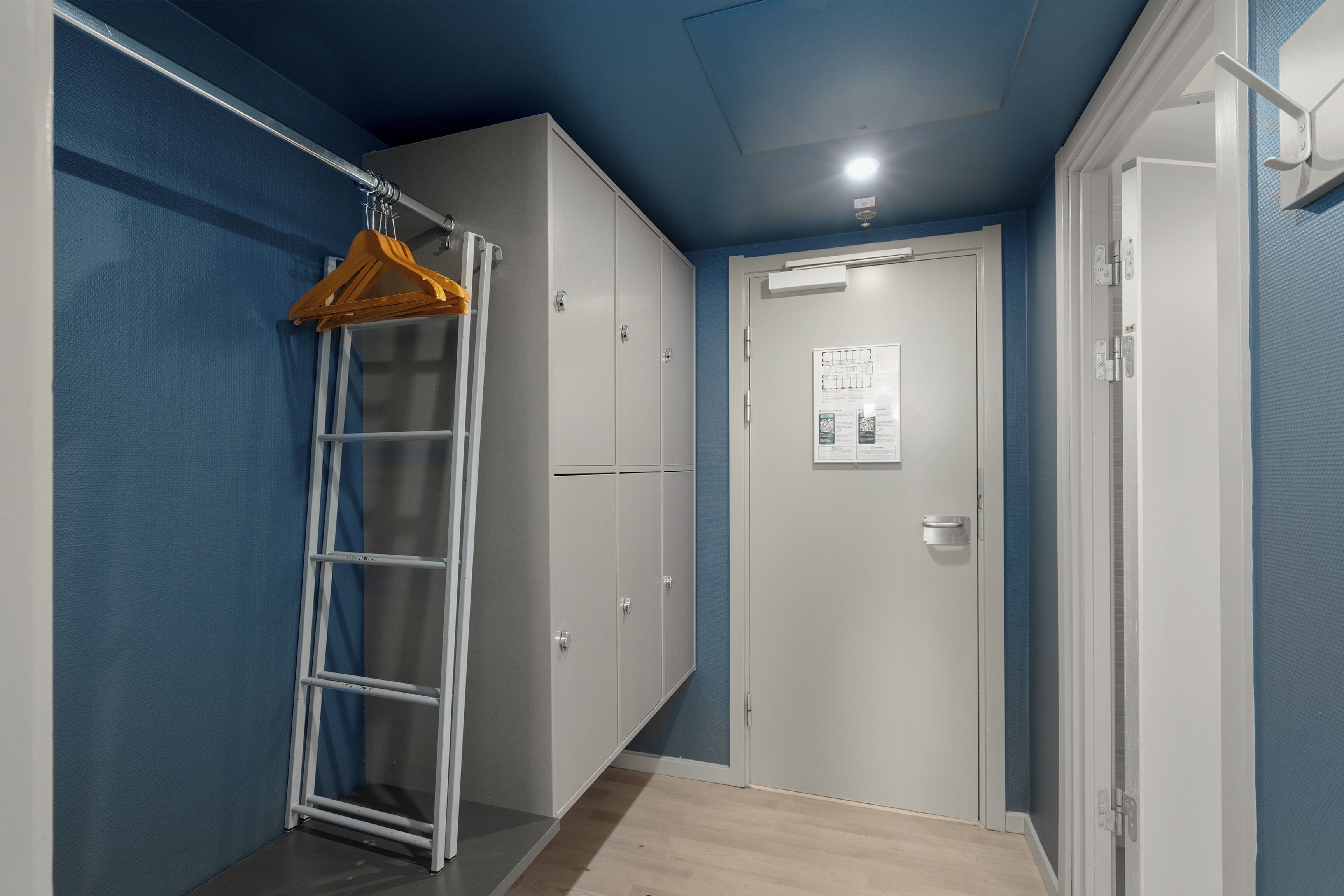 Un couloir avec une armoire blanche, une étagère en métal et une porte sur laquelle est affiché un avis.
