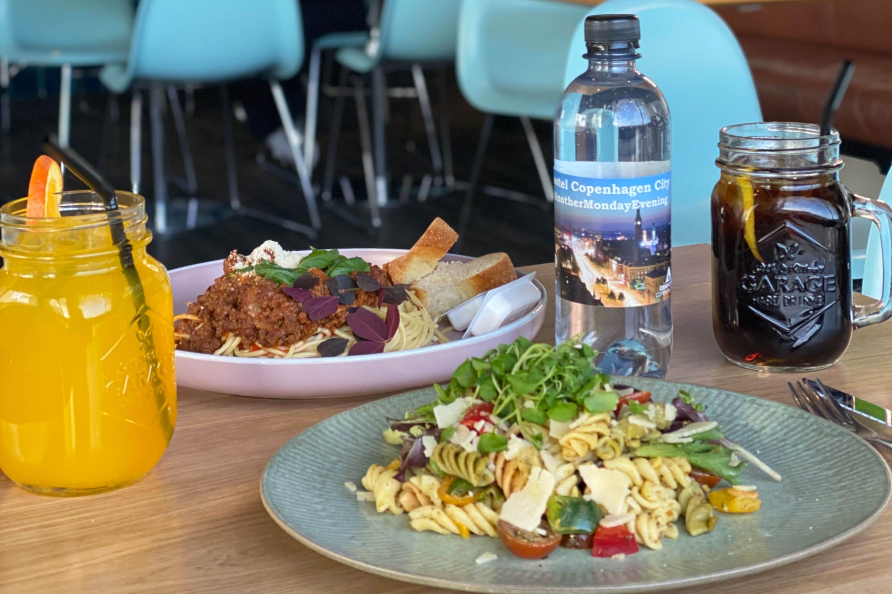 A table with two plates of food, a bottle of water, and a jar of sauce.