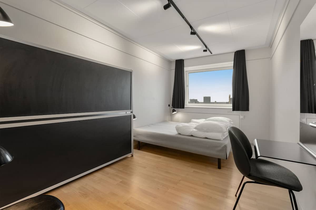 Une chambre d’hôtel moderne, équipée d’un lit, d’un bureau et d’une grande fenêtre.
