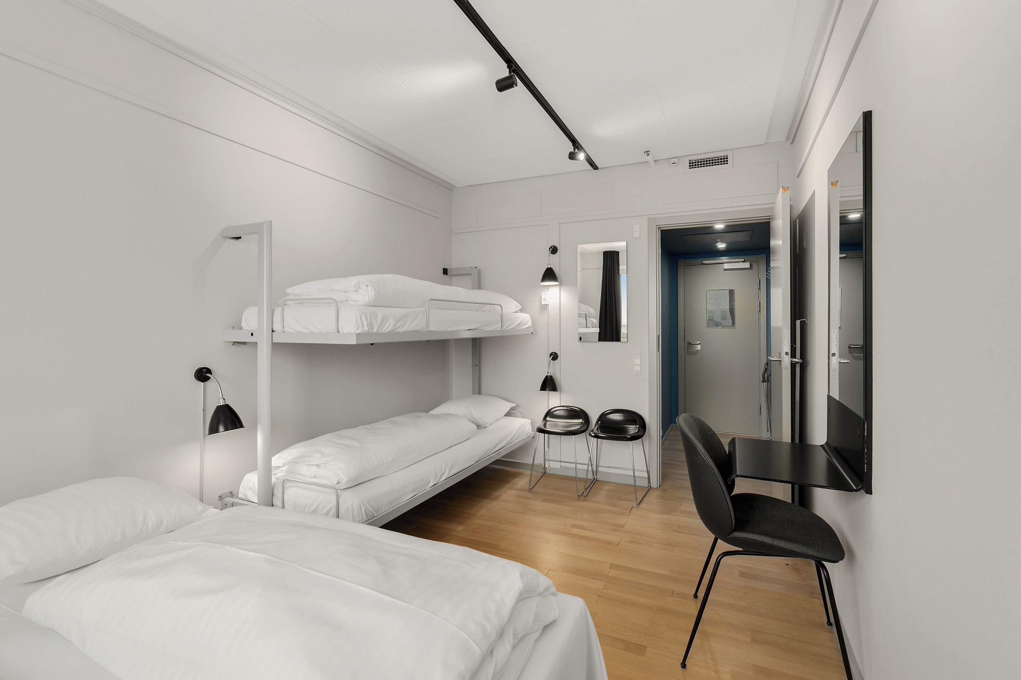 Una habitación de hotel moderna y minimalista con una cama litera, un escritorio y una silla.