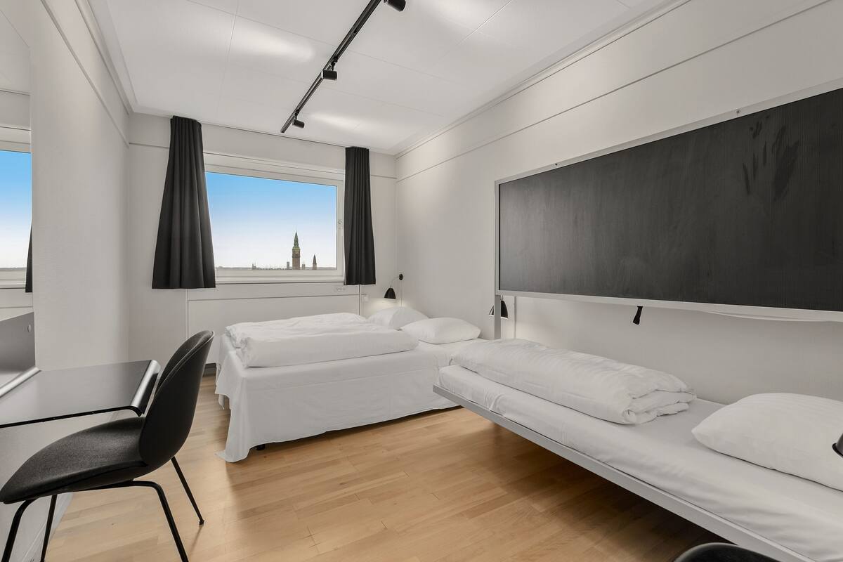 Une chambre d’hôtel moderne avec deux lits, un bureau et une vue sur le paysage urbain.