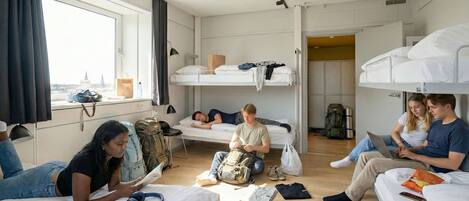 A dormitory-style room with bunk beds, a communal seating area, and a window with a view.