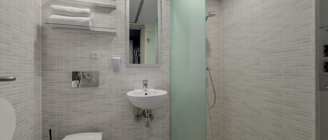 Un baño con paredes de azulejos blancos, un lavamanos blanco, un inodoro y un estante de vidrio con toallas.