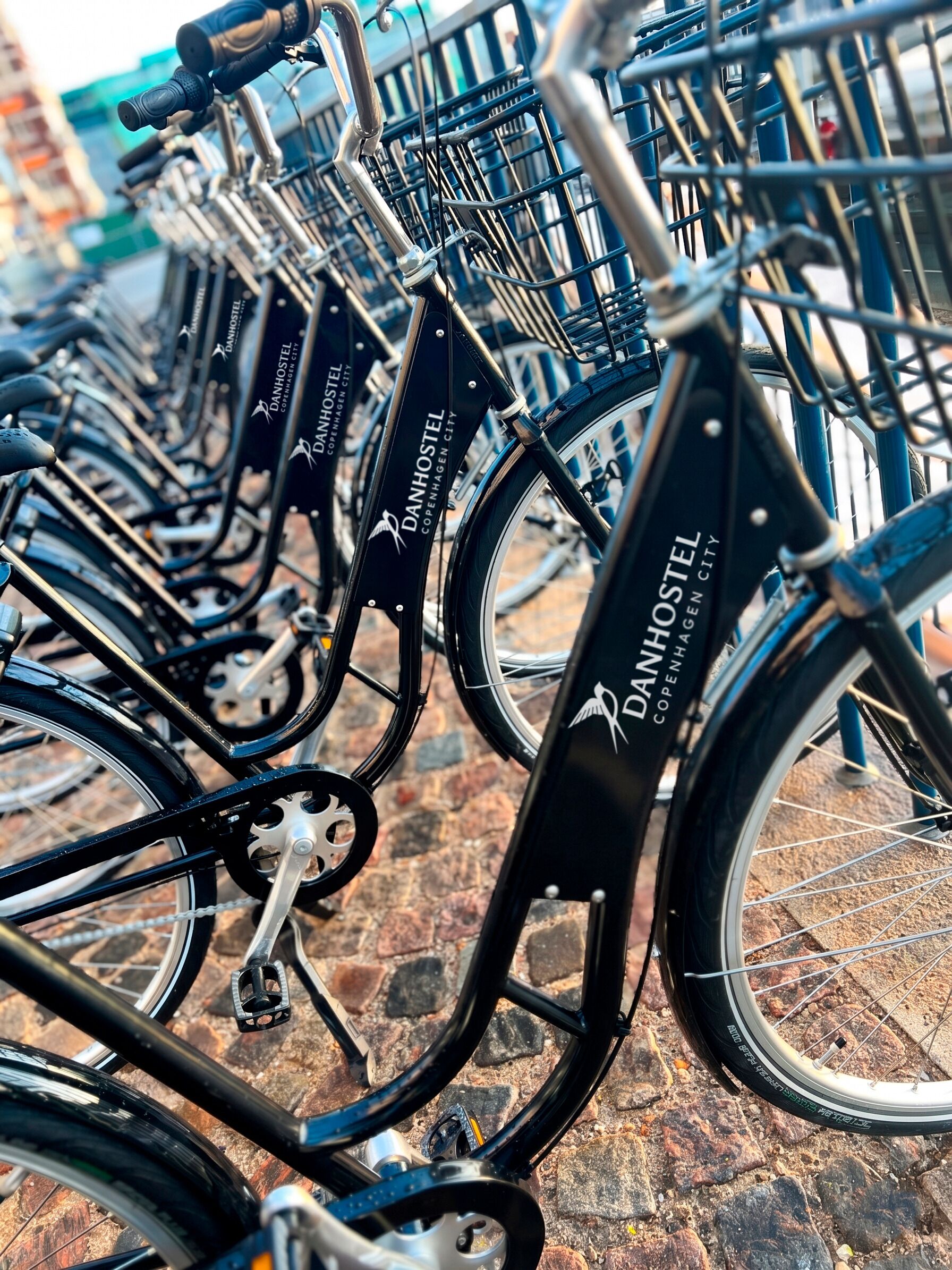 Een rij fietsen met de branding 'DANHOSTEL Copenhagen City', geparkeerd buiten.