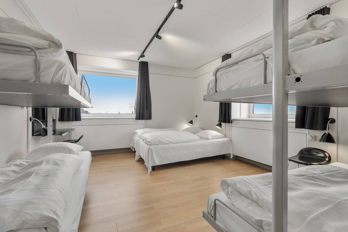 Une chambre d’hôtel moderne avec des lits superposés, une grande fenêtre et un bureau avec une chaise.
