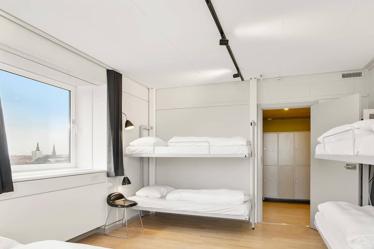 Une chambre avec un lit superposé offrant une vue sur la ville, un bureau avec une chaise et une armoire.