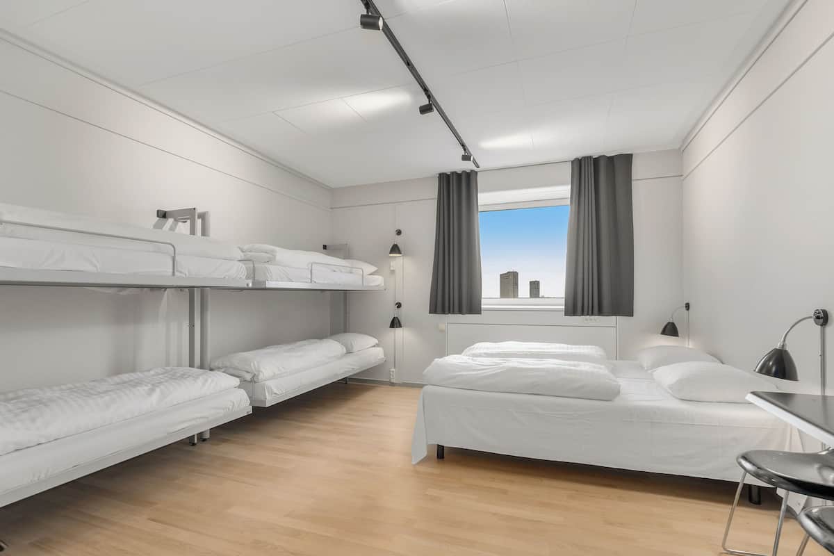 Une chambre d’hôtel avec des lits superposés, un bureau et une fenêtre avec des rideaux.