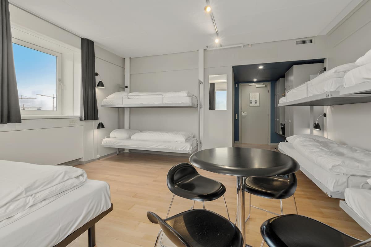 Une chambre d’hôtel avec des lits superposés, une table ronde avec quatre chaises et une fenêtre avec des rideaux.