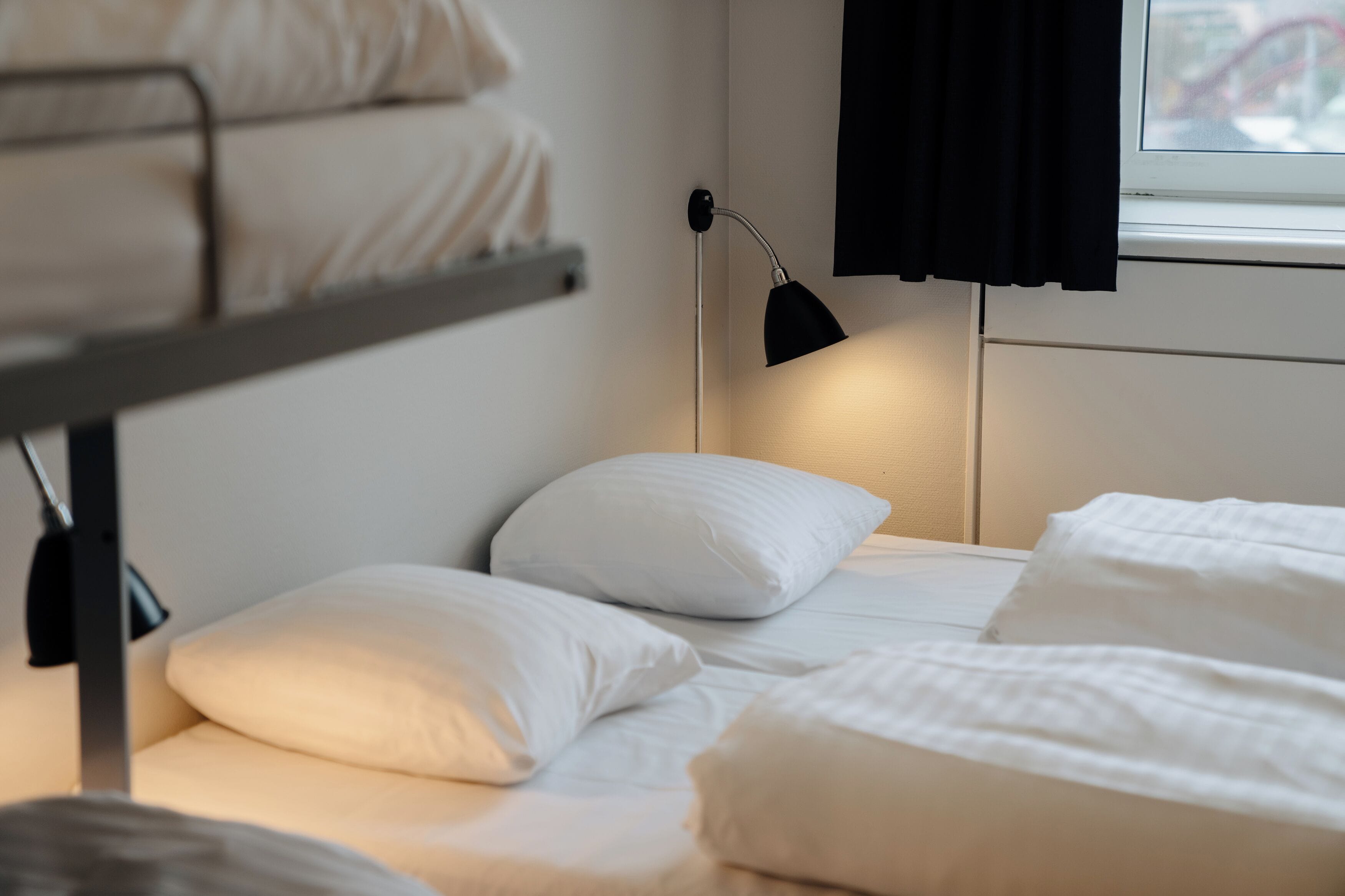 Una cama litera con ropa de cama blanca y una lámpara de noche.