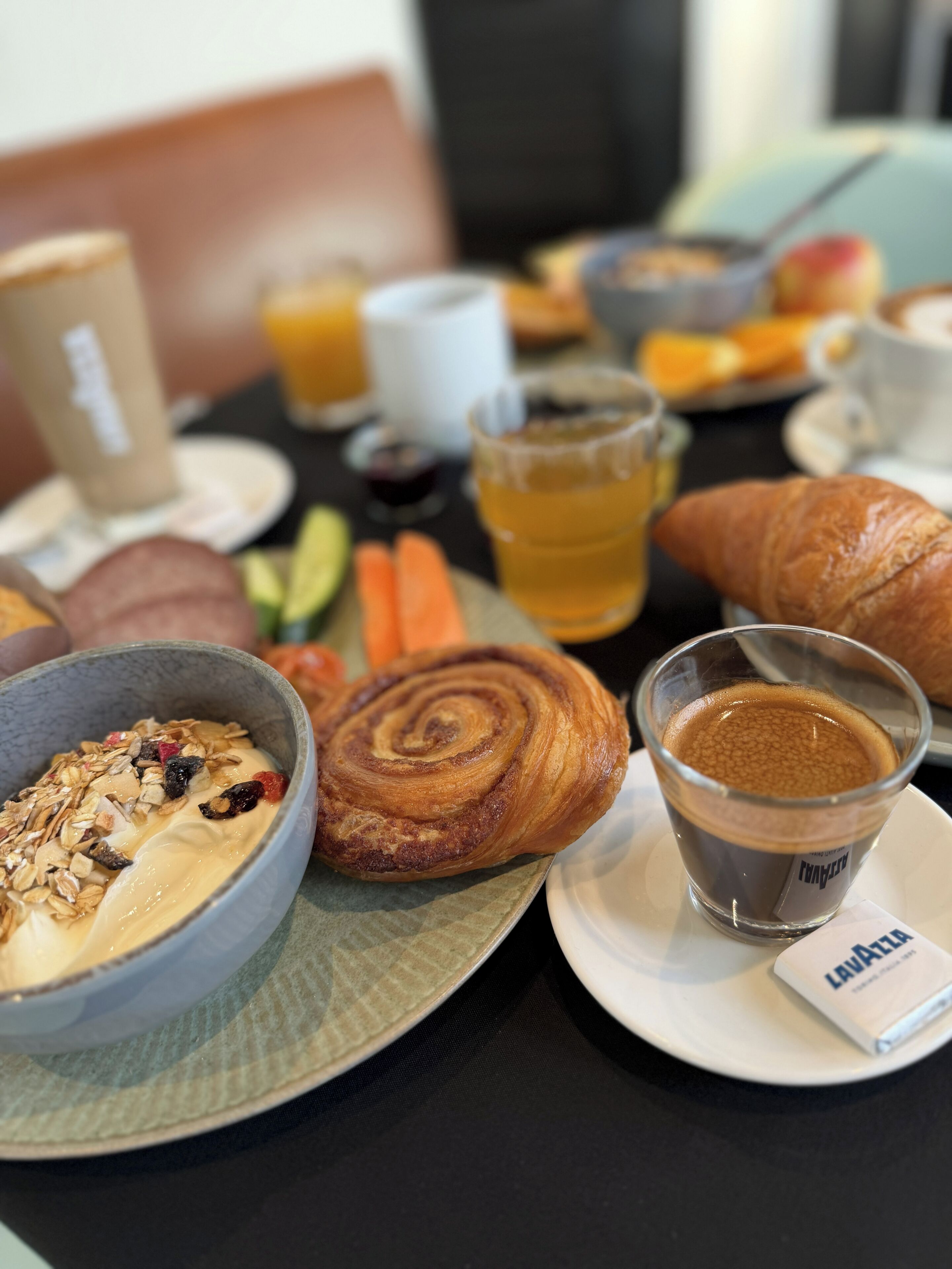 Ein Frühstückstisch mit einem Croissant, Kaffee, einer Schüssel Müsli und Obst.
