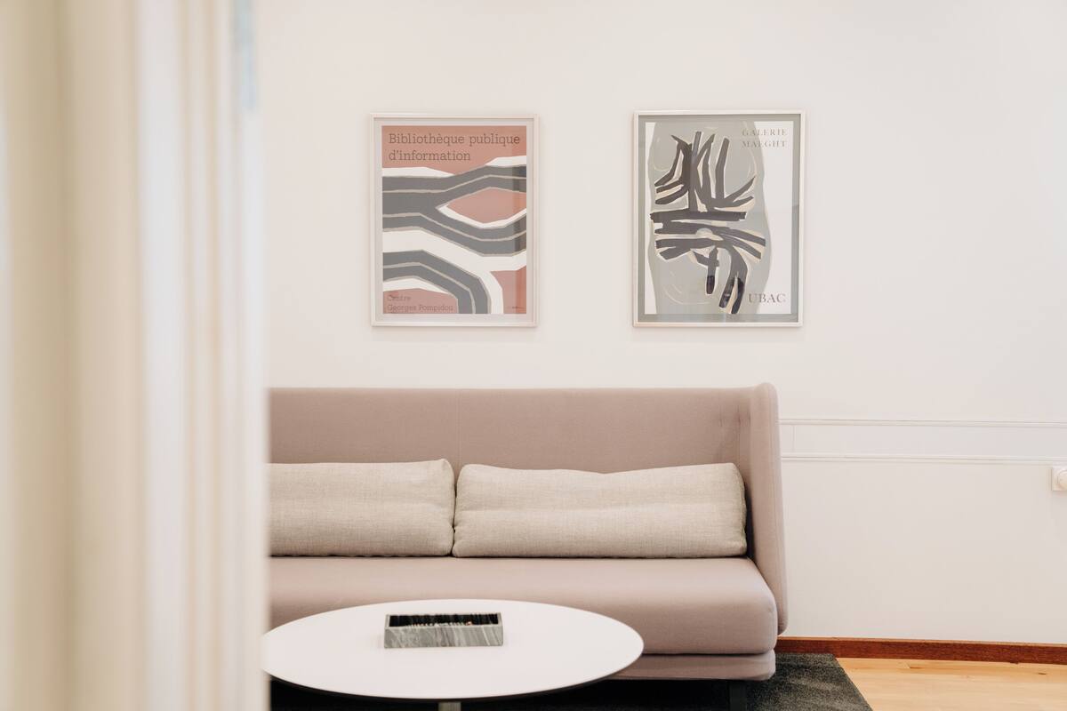 Un salon moderne avec un canapé beige, une table basse ronde blanche et deux œuvres d’art encadrées accrochées au mur.