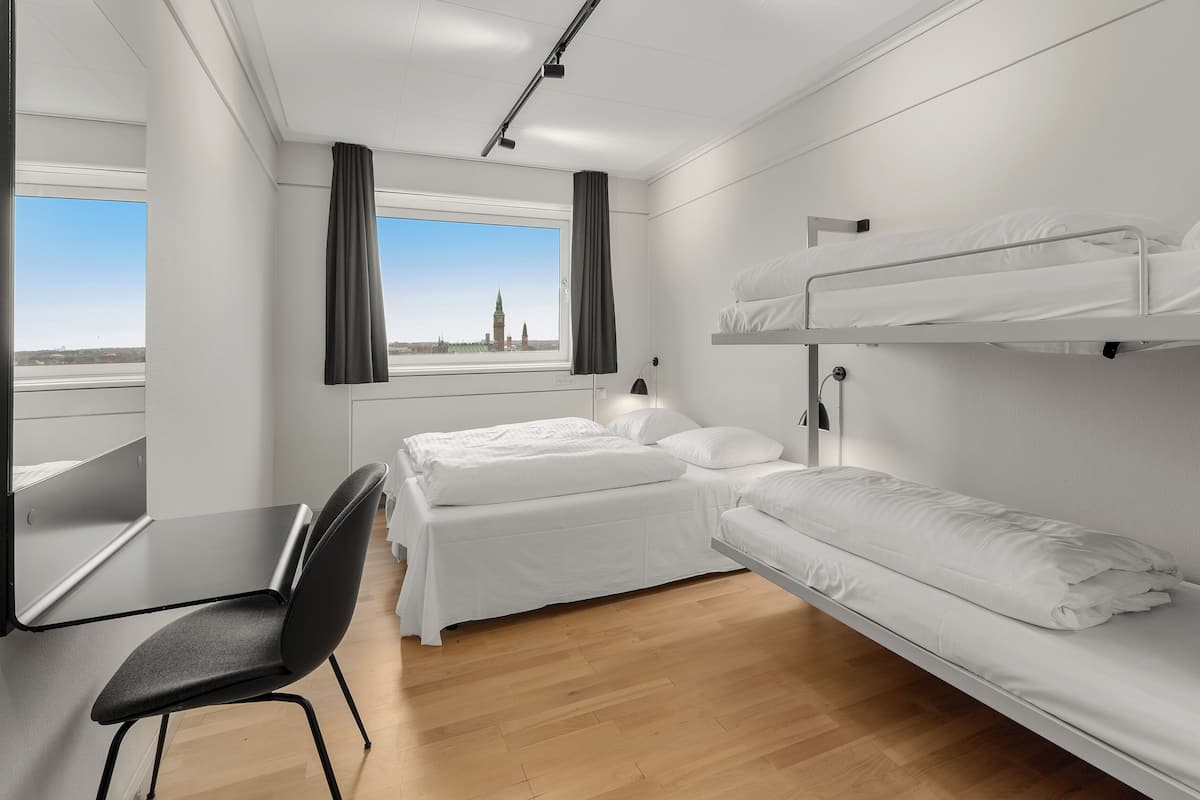 Une chambre d’hôtel avec un lit superposé, un bureau avec une chaise et une fenêtre avec des rideaux.