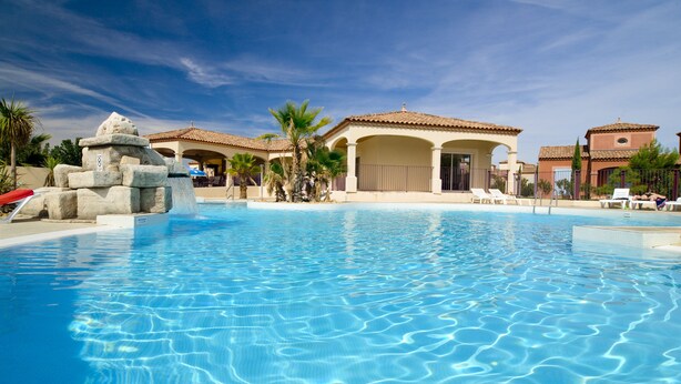 A clear blue swimming pool with lounge chairs and a stone structure.