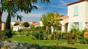 A row of Mediterranean-style buildings with terracotta roofs and light-colored walls, surrounded by well-maintained gardens and trees.