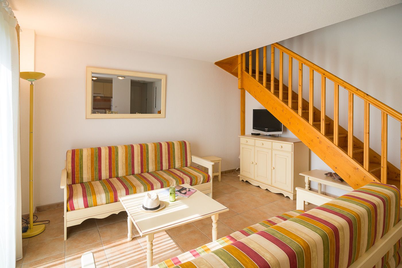 Ein gemütliches Wohnzimmer mit einem gestreiften Sofa, einem kleinen Tisch, einem Schrank und einer Holztreppe.