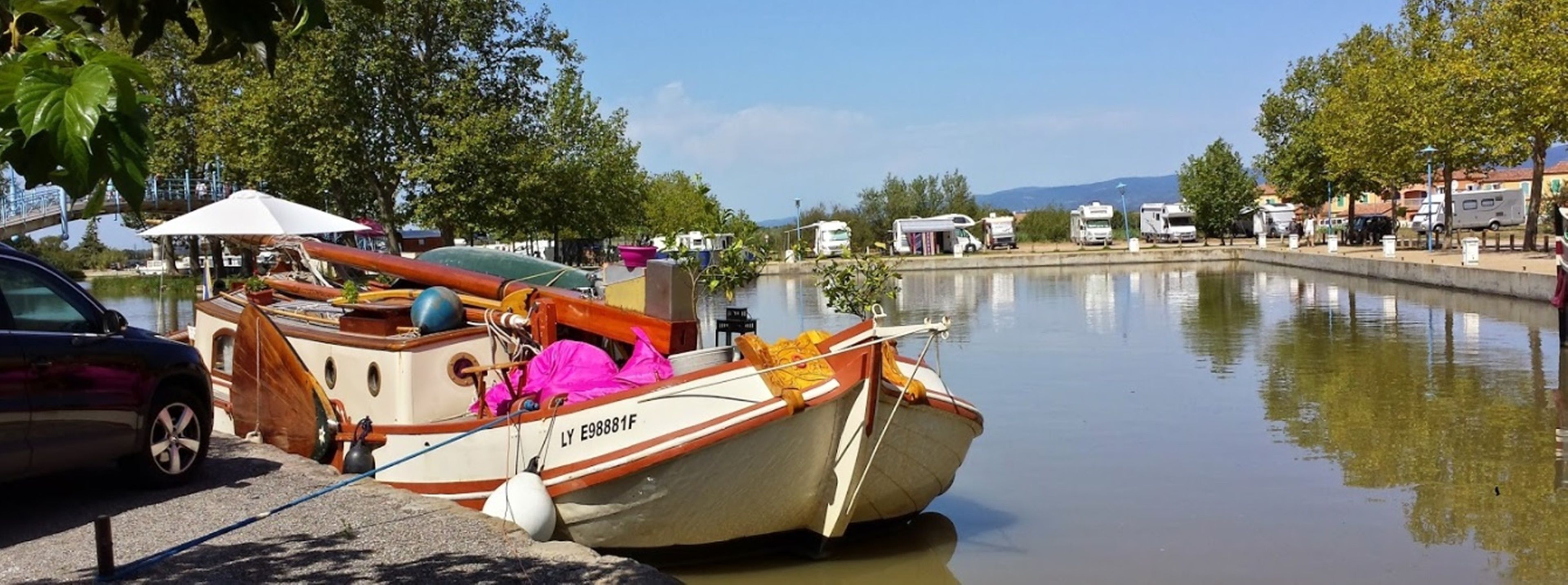 A small boat docked at a marina with a car parked nearby.