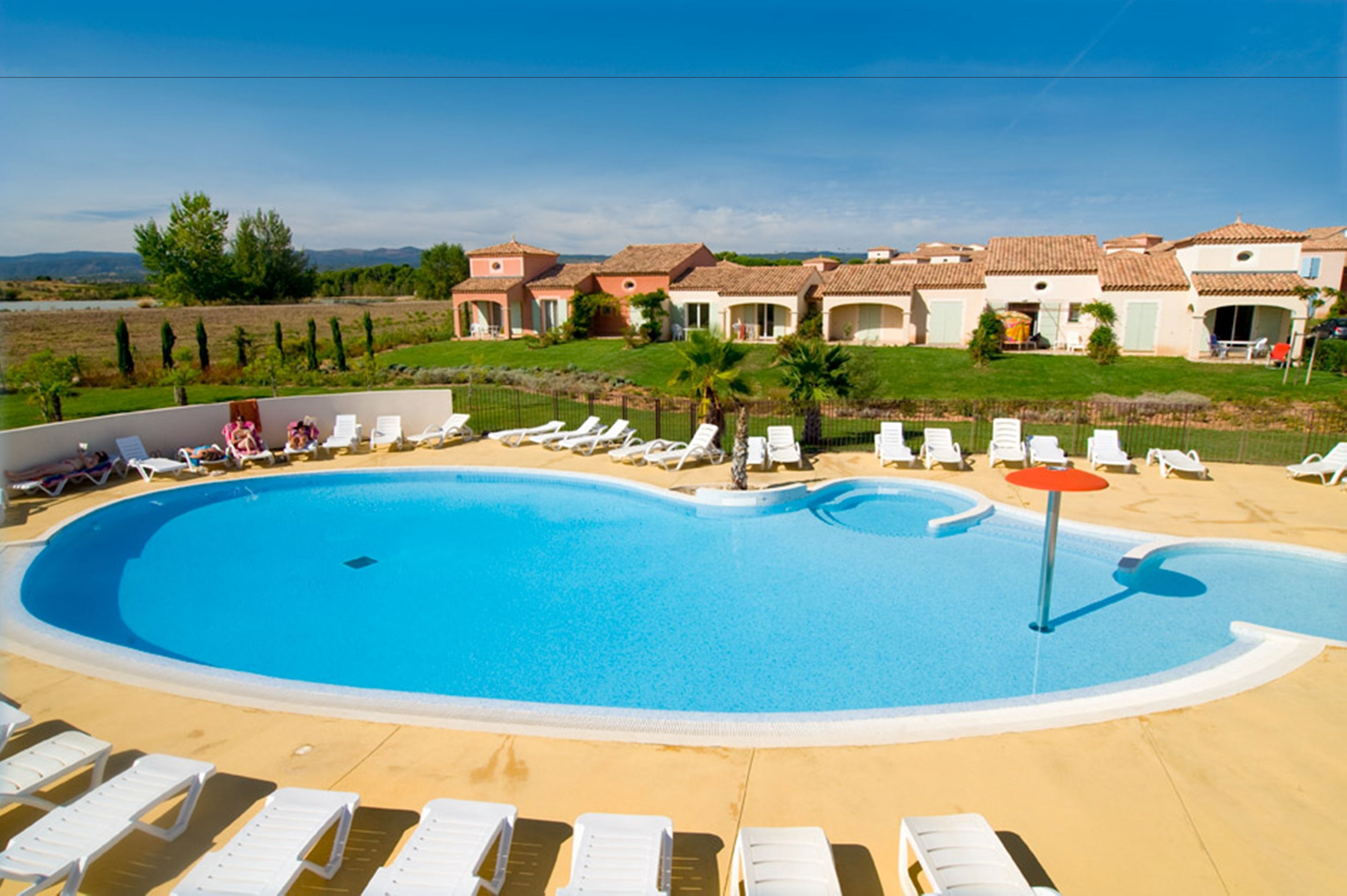 Piscina com espreguiçadeiras e vista para vilas ao fundo.
