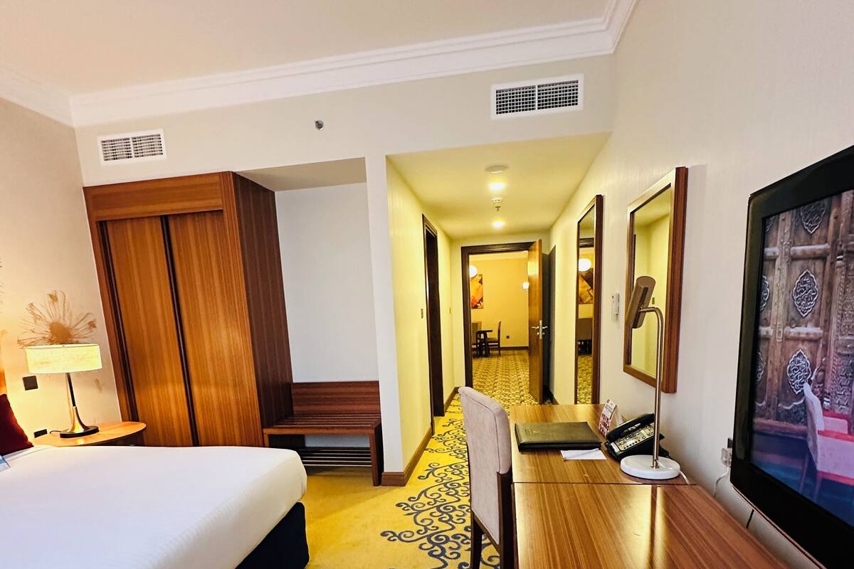 Una habitación de hotel con cama, escritorio, silla, lámpara, televisor y armario.