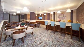 A hotel lobby with a bar area, dining tables, and chairs.