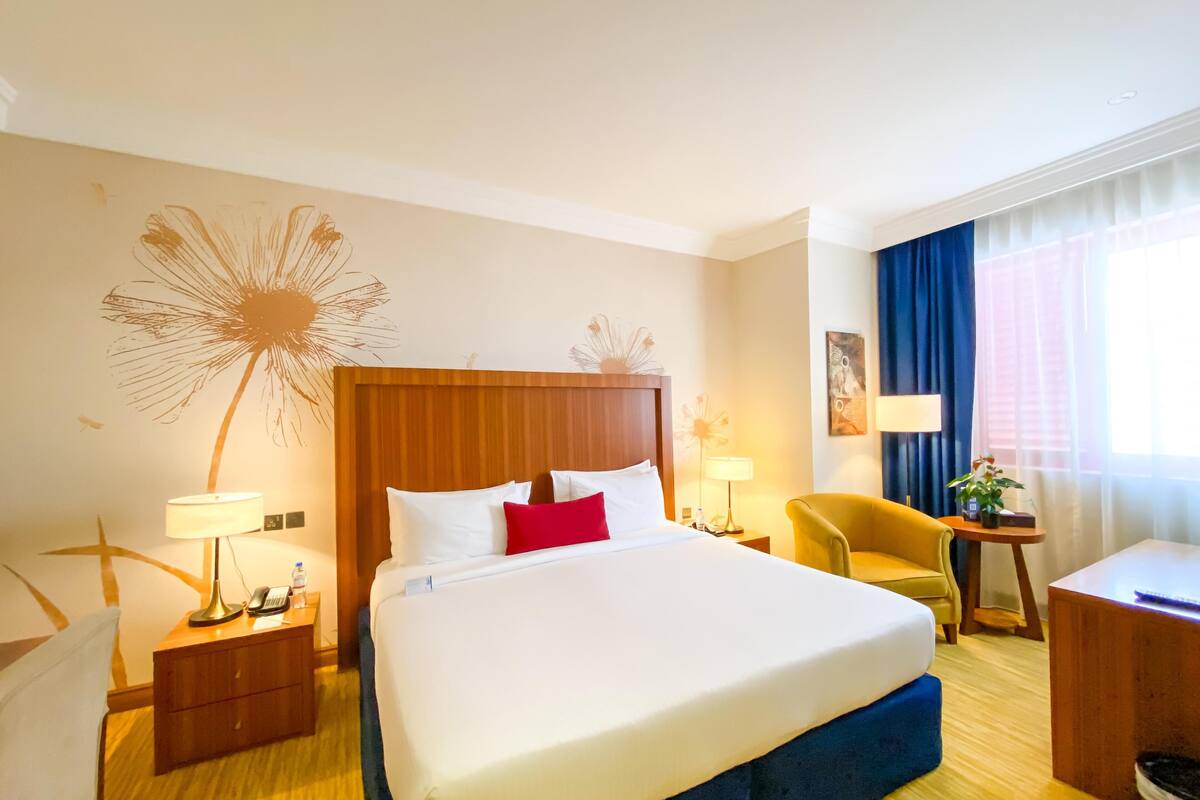 Una habitación de hotel con una cama grande, mesitas de noche con lámparas, una silla, un escritorio y una ventana con cortinas.