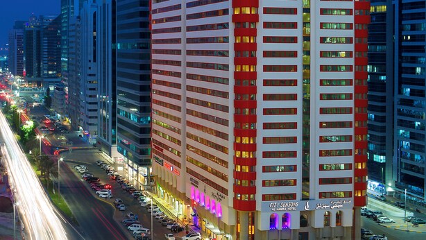 Un hotel moderno de gran altura con varias plantas, un letrero llamativo y una calle concurrida con semáforos.