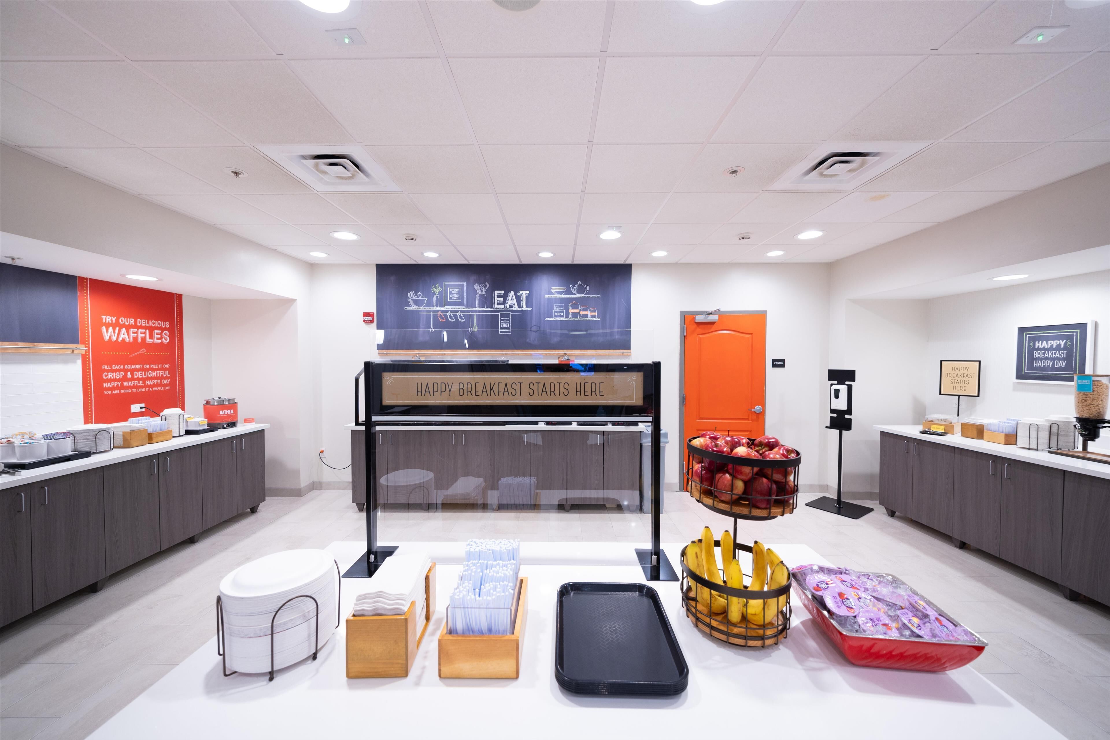 A breakfast area with a chalkboard sign, a fruit display, and a waffle station.