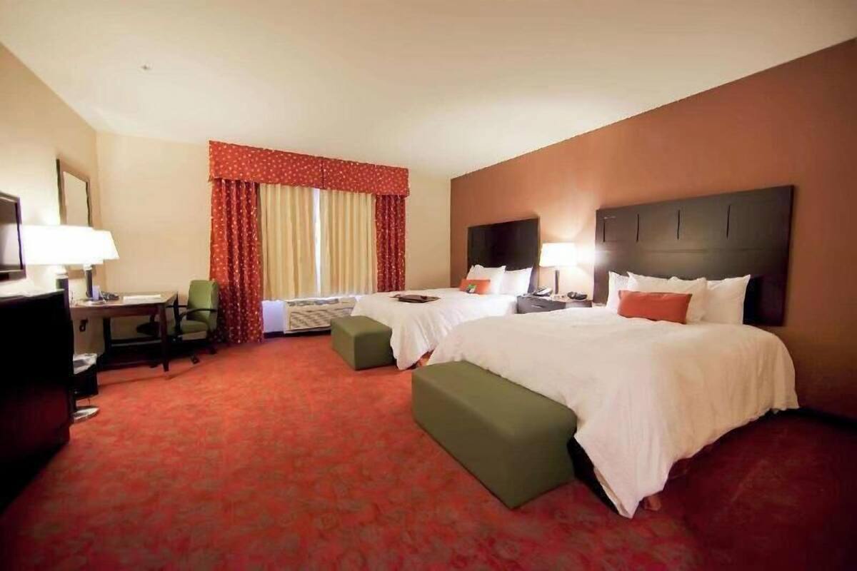 A hotel room with two beds, a desk, a chair, and a television.