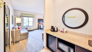 A modern hotel room with a kitchenette, a large mirror, a sofa, and a window providing a view of the outdoors. - Hampton Inn & Suites Seattle/Kent,WA (Kent)