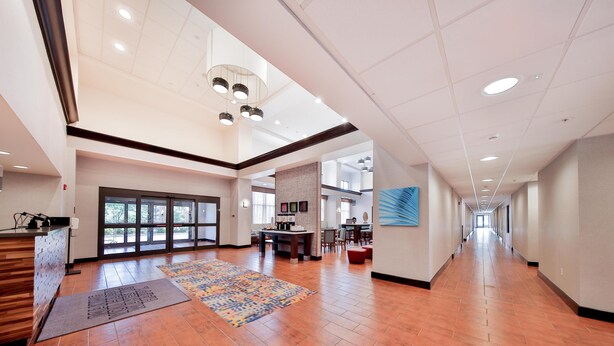A spacious hotel lobby with a wooden reception desk, a patterned rug, and a long corridor leading to a dining area. - Hampton Inn & Suites Seattle/Kent,WA (Kent)
